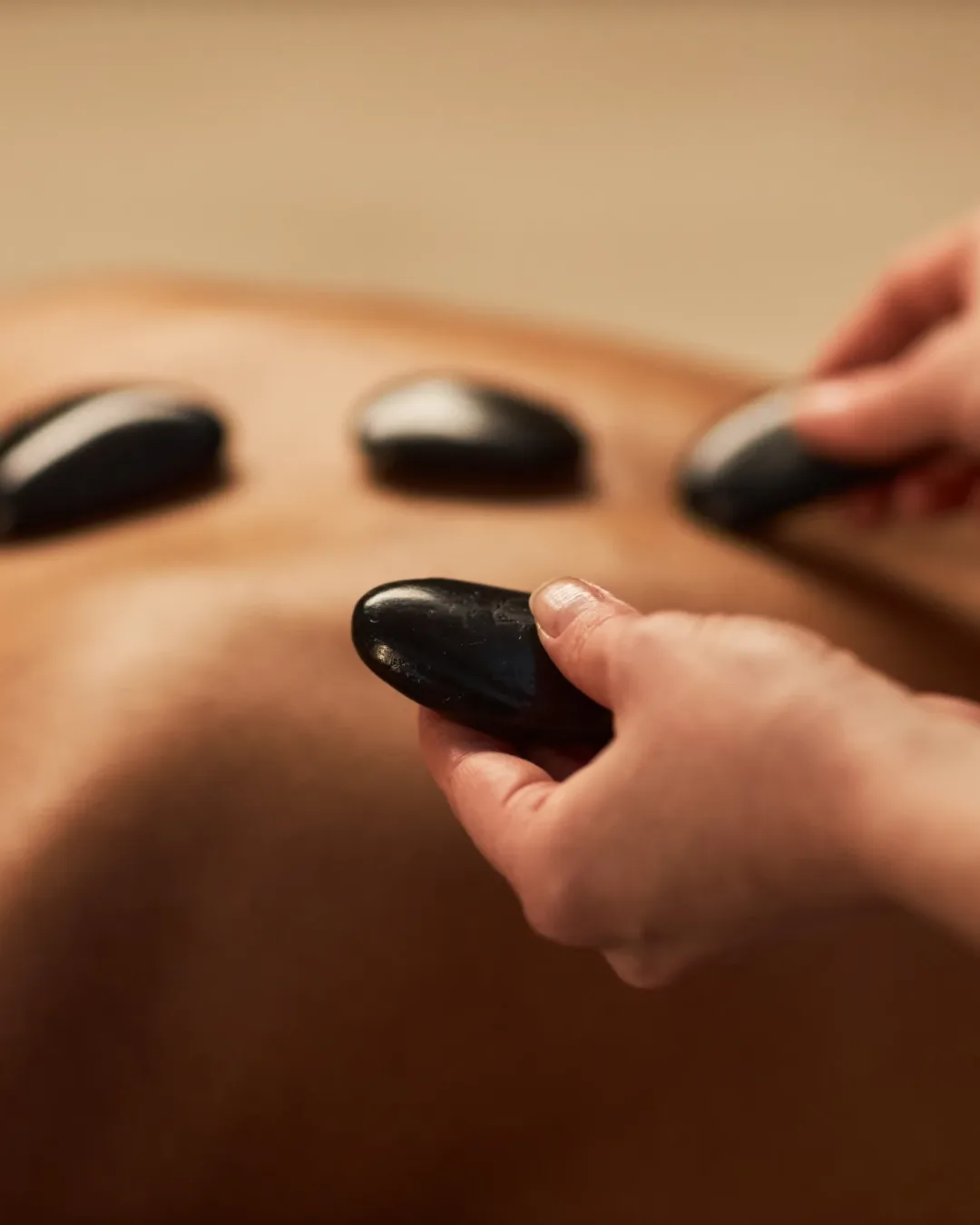 Spa therapist putting hot stones on back of young woman