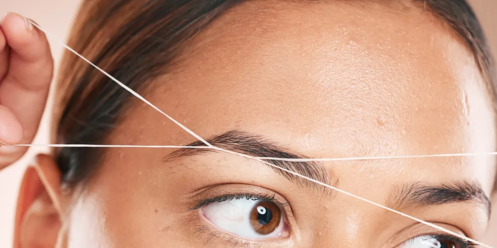 Threading, eyebrows and beauty with a model black woman in studio on a beige background for hair removal. Eyes, zoom and wellness with an attractive young female using a product on her face.